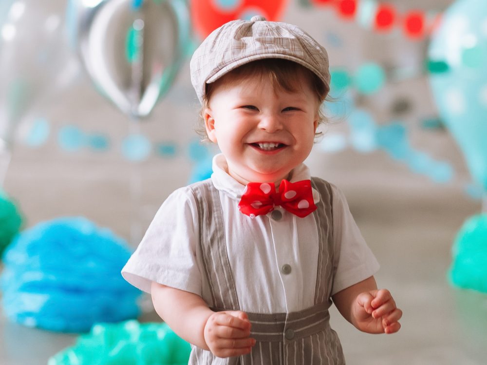 Happy baby boy celebrating first birthday. Kids birthday party decorated with balloons and colorful banner.